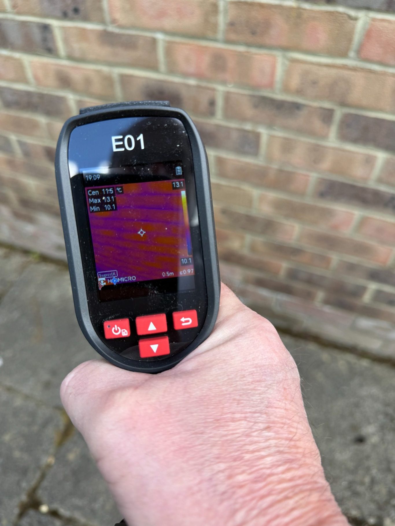 Handheld thermal imaging camera displaying temperature readings on its screen.